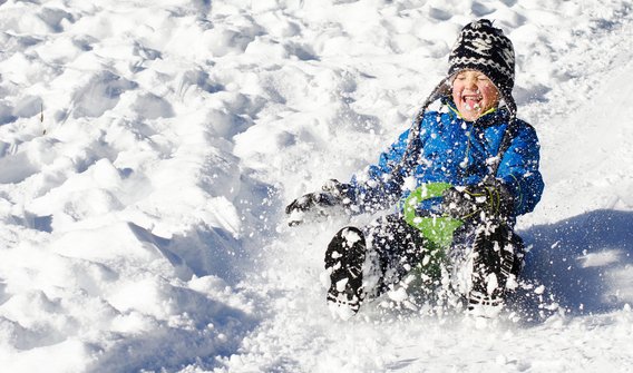 Bild: Ein kleines Kind, welches im Winter einen Berg hinunter rodelt 